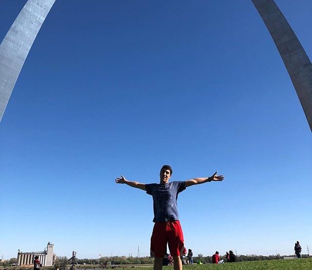 Adam standing with arms stretched out under the St. Louis Arch